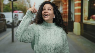 Dışarıyı gösteren kadın süveter giymiş, güler yüzlü, gülen bir kadın. Sonbahara bakıyor, hayat dolu bir sokak hayatı kuruyor. Neşeli şehir geçmişini yakalıyor.