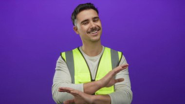 Yalıtılmış mor arka plan duvarının önünde elleri ile yansıtıcı yelek jestler giyen genç adam görünüşe göre oyuncu ya da küçümseyici bir şekilde.