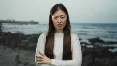 Kumsalda duran, uzun saçlı, duygularını ifade eden, beyaz gömlek giyen, açık hava, genç, yetişkin, Asyalı, güzel bir kadın..