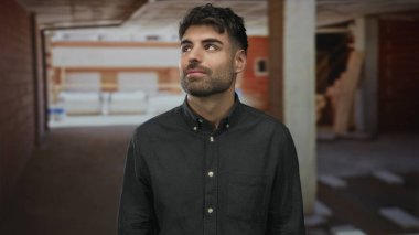 Yapım aşamasında olan binadaki tamamlanmamış tuğla duvara yüzünü gösteren adam gülümsüyor..