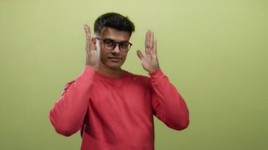 Kırmızı gömlekli genç adam, münferit bir portre oturumunda yaratıcılığını ve pozitifliğini ifade eden sarı arka planda ellerini kullanarak çerçeveleme hareketi yapıyor.