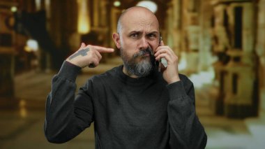 Müzede sakallı, telefonda konuşan kel bir adam evde el hareketleriyle hayal kırıklığını gösteriyor. Stres iletişimi kurarken kafkasyalı erkek dövmesi yaptırıyor..
