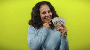 Meksika pezosu tutan orta yaşlı bir kadın sarı arka plana gülümsüyor, para ve kültürel bağlam gösteriyor..