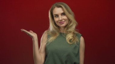 Gülümseyen ve avucuna işaret eden genç bir kadın canlı kırmızı bir arka plan, pozitiflik ve güven ifade ediyor.