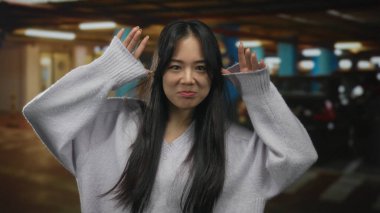 Kapalı otoparkta arabalarla gülümseyen Çinli genç bir kadın, parlak yapay ışıklar altında neşeli davranışlar sergiliyor..