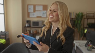 Ofisteki sarışın kadın, elinde profesyonel kıyafetlerle gülümseyen bir tablet tutuyor. Teknoloji ve iş hayatına odaklanmış üretkenlik ve modern iş ortamını öneriyor..