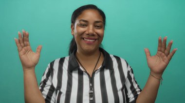 Hakem, stüdyoda siyah-beyaz çizgili forma ve ıslık ipi giyerek başının yanında el kaldırıyor..