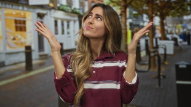 Kadın omuz silkme hareketi için kaldırılır yaya alışveriş caddesinde çizgili polo gömlek giyerek; kafa karışıklığı şüphe kararsızlık.