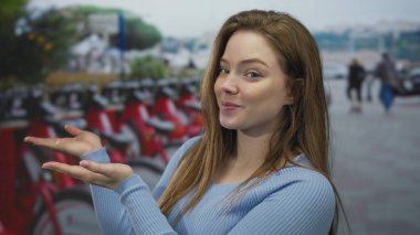 Şehir caddesinde kırmızı kiralık bisiklet sırasının önünde el ele tutuşan genç bir kadın. Macera merakı..