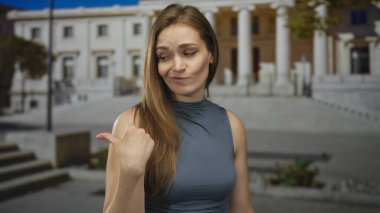 Parlak güneş ışığı altında sütunları olan neoklasik bir binanın yakınındaki boş sokağa başparmağını gösteren kadın; kayıtsızlık.