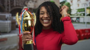 Kadın kupa tutuyor ve sokakta gülümserken yumruk pompalıyor; zafer sevinç güçlenmesini kutluyor.