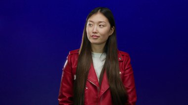 Kırmızı ceketli kadın izole edilmiş mavi arka planda duruyor. Uzun saçlı ve günlük kıyafetleri olan çekici Asyalı bir kadın var..