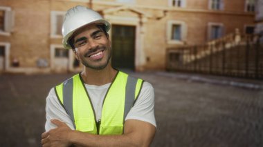 Beyaz şapka takan İspanyol bir adam ve eski bir kasaba binasının önünde kollarını kavuşturmuş sarı güvenlik yeleği giyen bir adam..