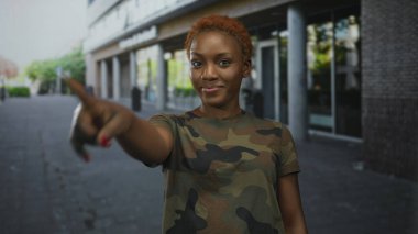Kadın asker şehir caddesinde dikilirken kamerayı işaret ediyor..