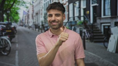 Pembe tişörtlü İspanyol adam parmaklarını kenarda gezdiriyor ve park halindeki bisikletlerle şehir caddesinde başparmak kaldırıyor. Onaylandı..