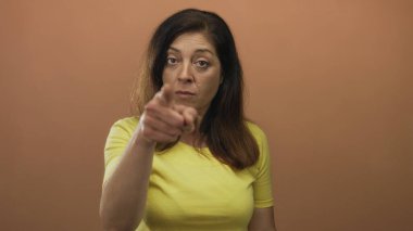 Şeftali stüdyosundaki kadın sert bir ifadeyle kamerayı işaret ediyor; sıkı komuta otoritesi aciliyeti.