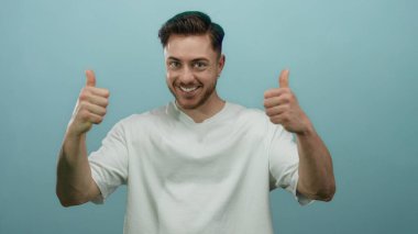 Parmakla gülümseyen genç bir adam canlı mavi bir arka plana karşı bir jest, izole edilmiş bir stüdyo ortamında pozitiflik ve güven yayıyor.