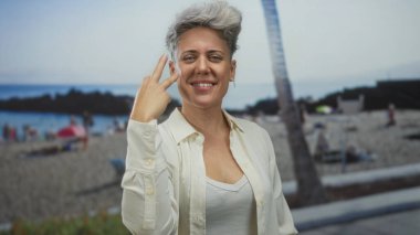 Kadın yumruklarını sıkar ve kameraya gülümser güneşli kumlu bir sahil kıyısındaki bir palmiye ağacının yanında zafer güçlendirir..