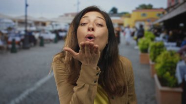 Kadın dudaklarını gösteren öpücük üflüyor ve meşgul sokakta açık el hareketi Kafe masaları ve saksı yeşillik ile sıralanmış; sıcak sevgi karşılama.