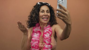 Mayolu İspanyol kadın ve Lei, izole olmuş kahverengi bir duvara selfie çekiyorlar. Orta yaşlı neşeli bir yaz havası sergiliyorlar..