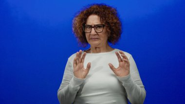 Mavi bir arka plana el kaldırarak tiksinen bir kadın basit bir ortamda net duygular sergiliyor..