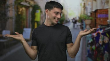 Siyah tişörtlü adam hem avuçlarını kaldırır hem de omuzlarını kaldırır ve arkasında bulanık bir kalabalık olur; belirsizlik.