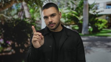 Siyah ceket giyen İspanyol bir adam yeşil bir parkta parmağını ileri doğru gösteren ciddi bir ifade var..