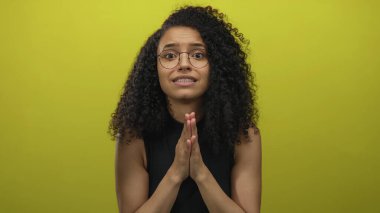 Genç İspanyol kadın, sarı bir duvarın üzerinden stüdyoda parmaklarını ovuşturarak endişeli bir bakış atar; çaresizce yardım için yalvarır..