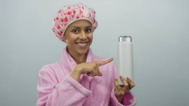 Pembe bornoz ve duş başlığı takan İspanyol bir kadın beyaz duvar arkasına karşı hoş bir jest yapıyor, rahat ve neşeli bir güzellik gösterisi sergiliyor..