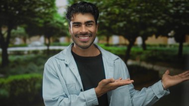 Yeşil parkta, ağaçların ve yürüyüş yollarının arasında açık palmiyeler sunan genç adam, neşeyi davet et..