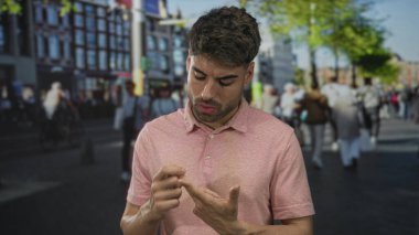 Pembe polo tişört giyen genç İspanyol adam, kalabalık bir sokakta işaret parmağıyla işaret parmağıyla işaret ediyor..