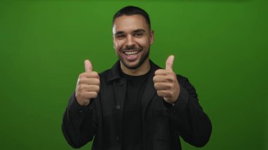 Genç İspanyol adam kapalı gözlerle gülümsüyor ve yeşil stüdyo ortamında iki kez onay veriyor..