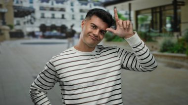 Striptiz tişörtlü genç adam şehir sokaklarında komik jestler yapıyor modern mimari arka planda şakacı davranışlar sergiliyor açık hava kentsel çevre portresi yakışıklı.