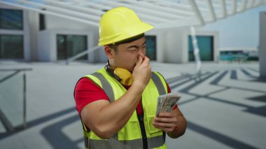 İnşaat malzemeleri giymiş genç bir adam bize dolar tutuyor ve şehir sokaklarında burun çimdikliyor. Endüstriyel kentsel çevrede hoş olmayan bir koku olduğunu gösteriyor..