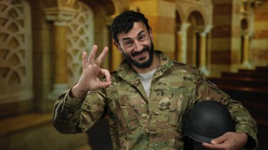 Askeri üniformalı ve sakallı bir adam katolik kilise ortamında, dekoratif mimari ile çevrili bir ortamda, güven duygusunu dile getiriyor..