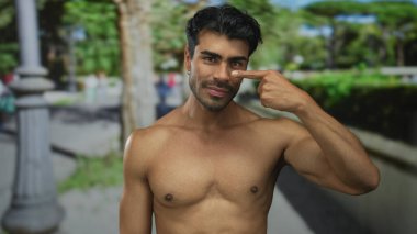 Gömleksiz İspanyol adam, güneş ışığı altında burun buruna orman yolunda yeşil ağaçları işaret ediyor..