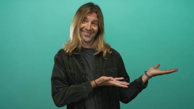 Sarışın ve uzun saçlı bir adam stüdyo ortamında avuçlarını açık bir şekilde sunuyor..