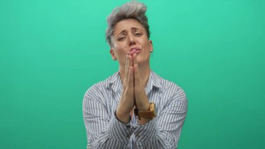 Nane yeşili stüdyo ortamında dua ederken kısa saçlı, çizgili gömlekli ve elleri bağlı bir kadın. Umut..