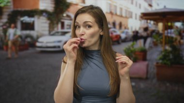 Mavi kolsuz bluzlu kadın, şehir caddesinde kafeterya çiftlikleriyle dolu dururken iki eliyle iyi bir hareket sergiliyor..