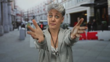 Gri kapüşonlu ve kolları çapraz gezen kollu bir kadın şehir caddesinde kendini kabullenmiş hissediyor..