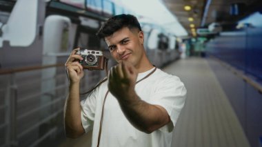 Bir yolcu gemisinde genç bir adam kamerayla şakacı hareketler yapar, açık hava macerasının ve boş zamanlarında yapılan seyahatlerin özünü yakalar, modern erkek stili ve ifadesini sergiler..