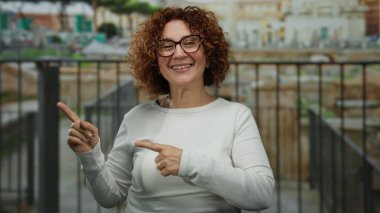 Antik Roma harabelerinin önünde gülümseyen bir kadın iki eliyle dışarıyı işaret ederek canlı bir şehirde tarihi bir cazibe ve kültür mirası sergiliyor..