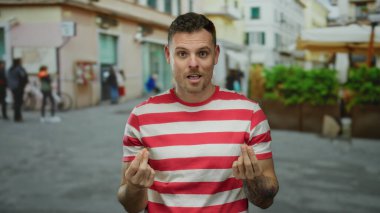 Çizgili gömlekli genç adam şehir sokağında para yapıyor. Arka planda bulanık insanlar şehir yaşamını yakalıyor..