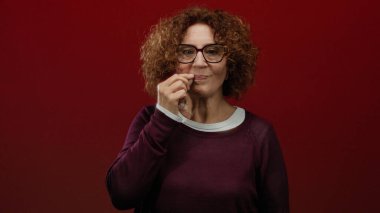 Esmer kadın, kültürel ifadelerini sergileyen canlı kırmızı duvara karşı sessizliğini gösteriyor..