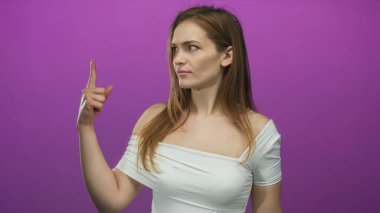 Mor stüdyo ortamında kamerayı yukarı doğru gösteren kadın ciddi bir ifadeyle işaret ediyor..