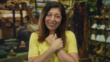 İspanyol orta yaşlı kadın giyim mağazasında ayakkabı askıları arasında gülümserken ellerini göğsünün üzerinden geçiriyor; rahatlık.