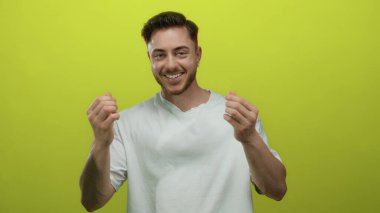 Genç sakallı beyaz adam, izole edilmiş sarı arka plana gülümseyip zenginlik ve mutluluk kavramlarını aktararak para hareketi yapıyor..