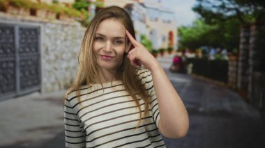 Yoğun bir şehir caddesinde, çizgili tişörtlü ve hafifçe sırıtan genç bir kadın, tefekkür.