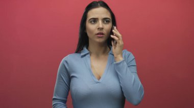 Mavi gömlekli İspanyol kadın kırmızı duvara karşı akıllı telefonla konuşuyor. Endişelerini ve duygularını dile getiriyor. Etkileyici bir iletişim ve içgözlem sahnesi yaratıyor..