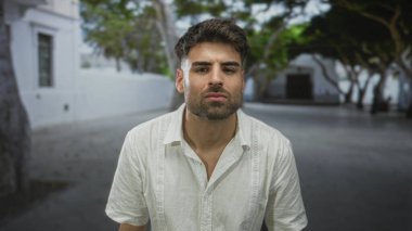 Erkek yüzü, ağaç gölgeliği ve parlak güneş ışığı altında şehir caddesinde beyaz gömlek giyerek yukarı bakıyor; iç düşünce.